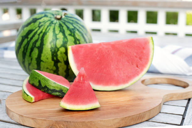 melancia e fatias em uma mesa no terraço de madeira. - watermelon melon fruit portion - fotografias e filmes do acervo