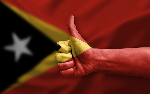 Hand making thumb up painted with flag of timor leste