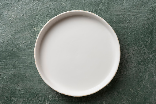 White ceramic empty plate on green vintage background, top view