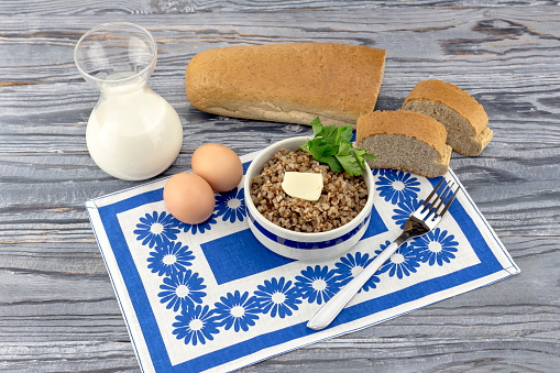 Buckwheat in a bowl, bread, eggs and milk in a jug on a table close-up