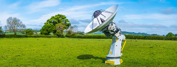 Radio telescope pointing at the heaven from a green field.