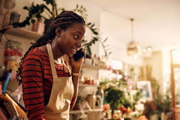 istock Black female florist talking on cell phone while working at flower shop. 1401396425