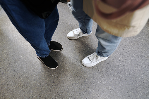 Legs in black and white sneakers stand side by side in the subway