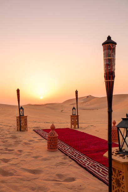 dîner dans le désert préparé pour le repas romantique au coucher du soleil dans les dunes de sable avec tapis et coussins - ras al khaimah photos et images de collection