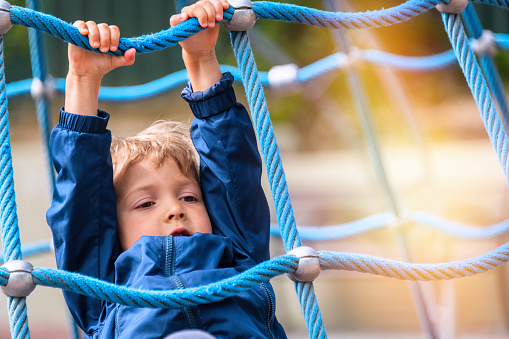 Caucasian Little boy hanging from robes at a schoolyard playground