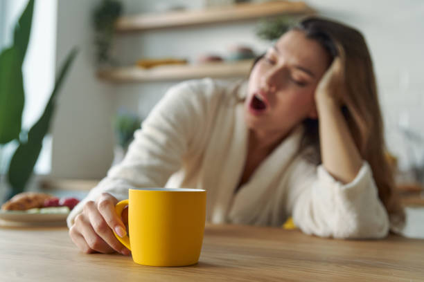 Young woman in bathrobe yawning with cup of coffee stock photo