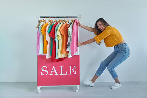 Cheerful young woman pulling a rack with colorful clothes