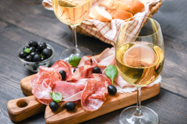 food antipasto prosciutto ham, salami, olives and bread sticks. charcuterie board. two glasses of white wine or prosecco - italian appetizer imagens e fotografias de stock