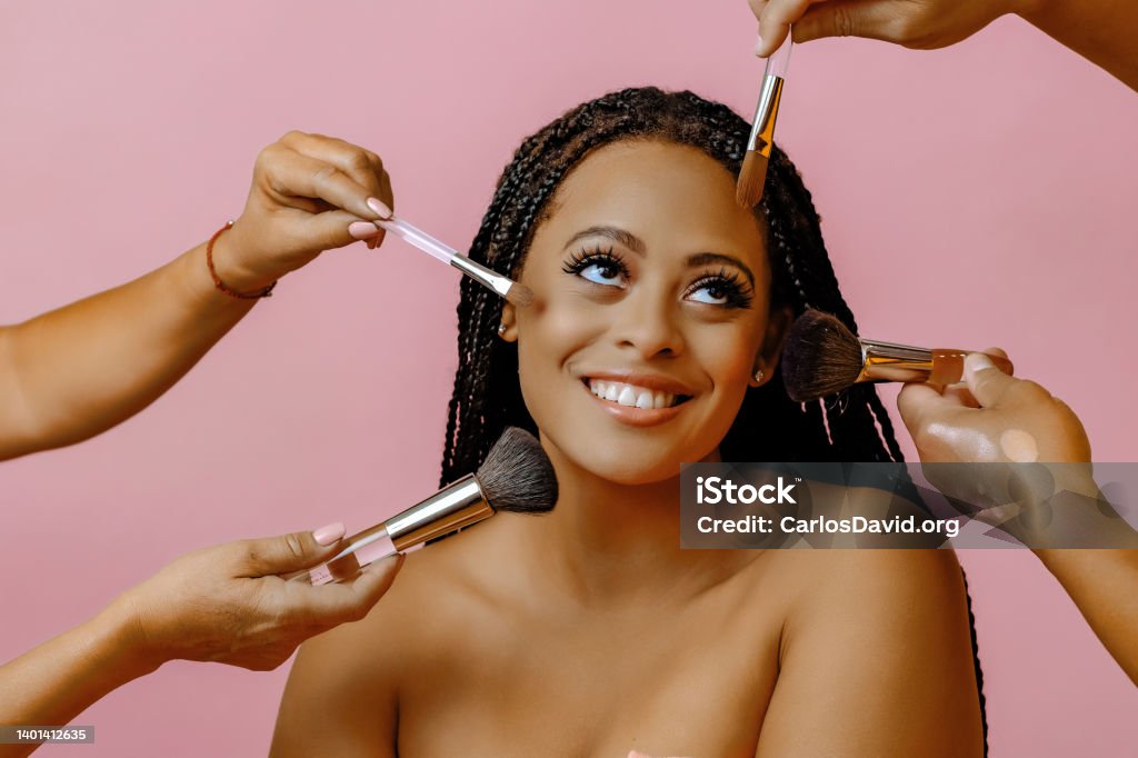 Happy smiling young adult woman with dreadlocks looking away at copy space on a pink background with hands holding makeup brush cosmetics around face Happy smiling young adult woman with dreadlocks looking away at copy space on a pink background with hands holding makeup brush cosmetics around face studio portrait Make-Up Stock Photo