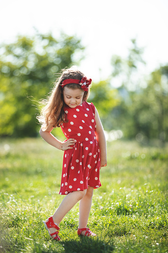 Portrait of a happy little blonde little girl in a red dress at public park