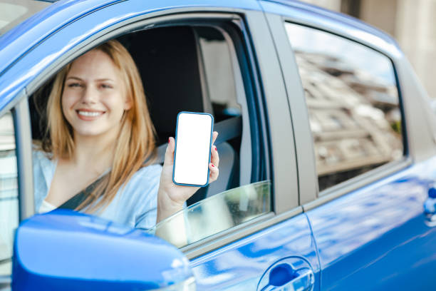 Young woman in a blue car showing empty smart phone screen stock photo