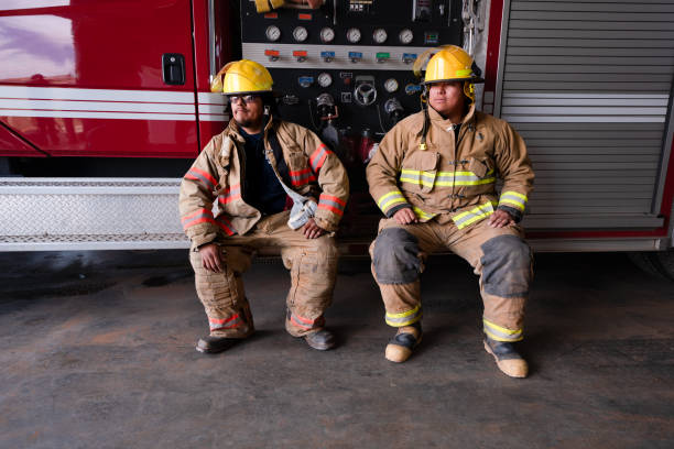 istock Two Confident Men Sitting On The Running Board Of A Fire Engine With Their Gear On,  Prepared For Assisting Any Kind Of  Emergency That Should Arise 1401422361