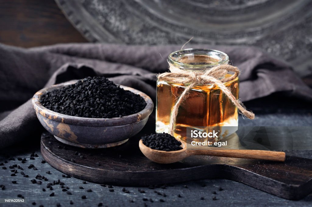 Black seeds in a bowl and oil Black seeds in a bowl and oil on a black background Nigella Stock Photo