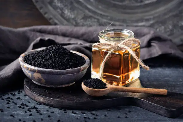 Black seeds in a bowl and oil on a black background