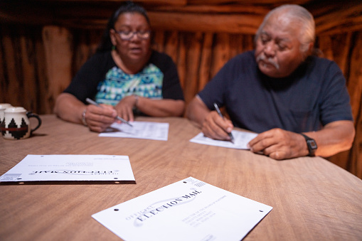 Navajo Senior Couple Sitting At A Table In Their Hogan, With Their Ballots, Looking Over The Voting Issues And Signing Their Ballots, Navajo Tribal Park, Monument Valley, Utah