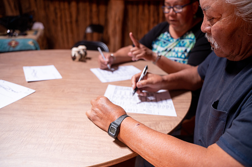 Navajo Senior Couple Sitting At A Table In Their Hogan, With Their Ballots, Looking Over The Voting Issues And Signing Their Ballots, Navajo Tribal Park, Monument Valley, Utah