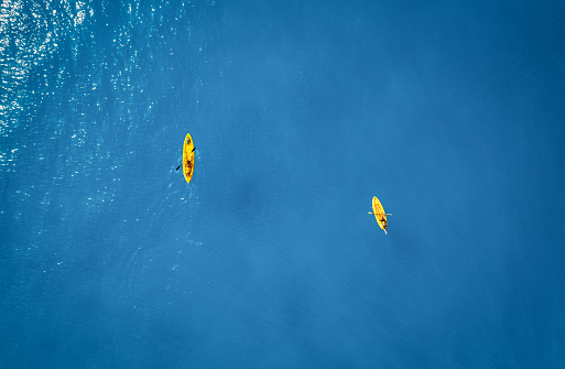 Aerial view of yellow kayaks in blue sea at sunset in summer. Man and woman on floating canoe in clear azure water. Lefkada island, Greece. Tropical landscape. Sup boards. Active travel. Top view