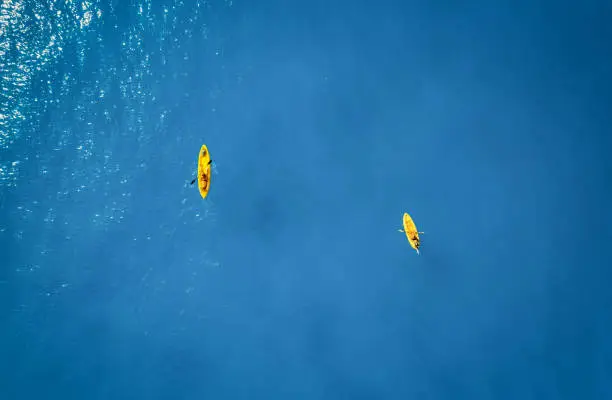Photo of Aerial view of yellow kayaks in blue sea at sunset in summer. Man and woman on floating canoe in clear azure water. Lefkada island, Greece. Tropical landscape. Sup boards. Active travel. Top view