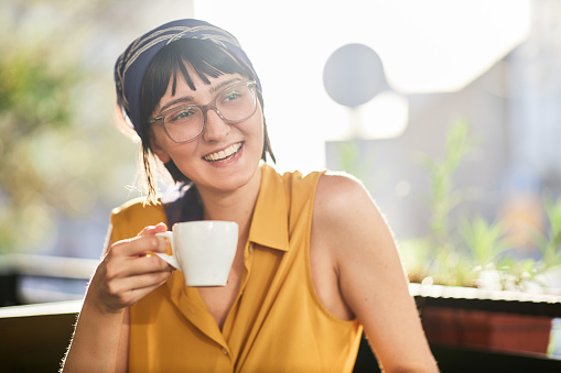 Cute young woman with glasses, holding a mug, sipping coffee in an outdoor coffee shop