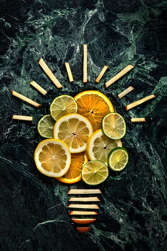 This is a conceptual photo related to the great idea of healthy eating using oranges, apples, lemons and limes and shaping them into the form of a light bulb on a green dark marble kitchen countertop