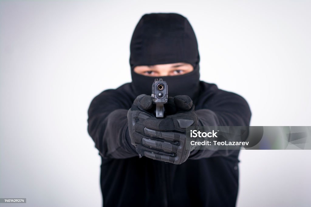 Gunman about to shoot with a gun Masked criminal, a fugitive, aiming with a couple of guns, studio image, white background Police Force Stock Photo