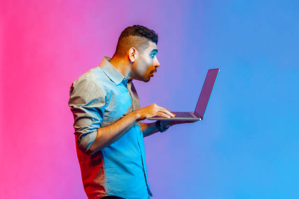 istock Side view of man typing email or surfing internet, looking surprised at laptop screen. 1401430255