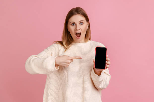 istock Astonished woman holding cell phone, pointing at smartphone display with copy space for promotion. 1401430350