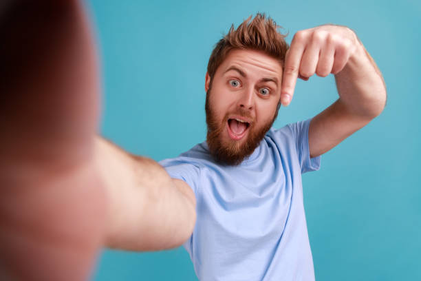 istock Man taking selfie or making video call, looking at camera POV, pointing finger down, subscribe. 1401432710