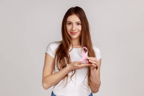 Happy smiling optimistic woman holding pink ribbon, symbol of breast cancer awareness. stock photo