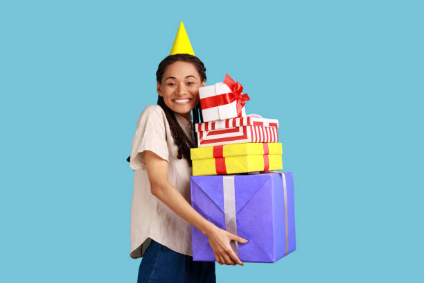 istock Happy woman with dreadlocks, posing in party cone, embracing stack of presents, celebrating birthday 1401433493