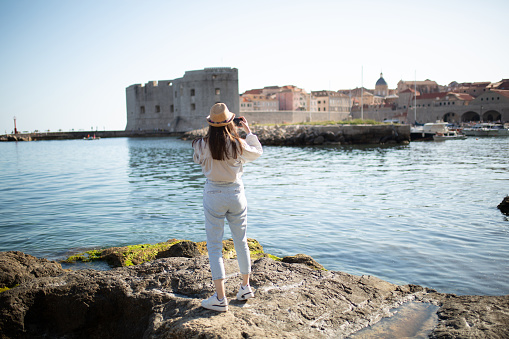 Beautiful girl taking pictures of St. John Fortress, Dubrovnik, Croatia with a smartphone.