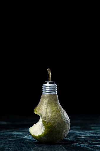 This is a conceptual photo blending a light bulb and a pear together on a dark background with green marble