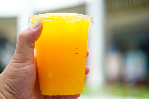 Hand holding orange juice in a plastic glass, summer drink.