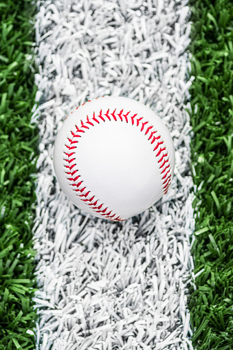 A high angle view of a new baseball sitting on the white baseline of a baseball diamond