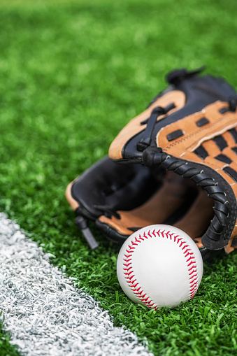 A new baseball and a brown leather glove sitting on the turf next to the white baseline of a baseball diamond