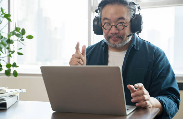 Asian middle aged man sitting at home working on video call. Work from home concept stock photo