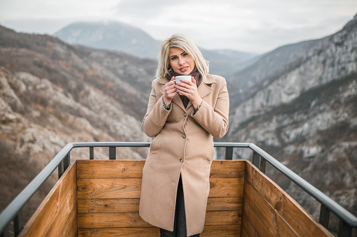 Gorgeous blonde woman standing on top of a mountain on cold winter day.
