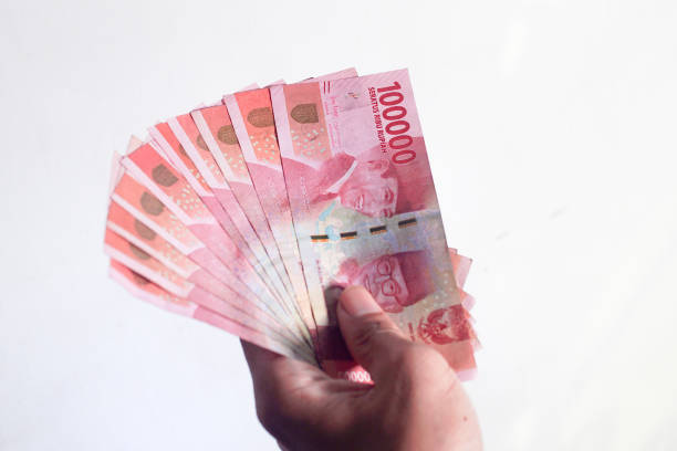 istock Hand holding and counting Indonesean Rupiah (IDR) bank notes with green background 1401448187
