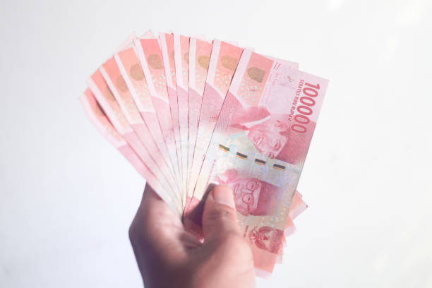 istock Hand holding and counting Indonesean Rupiah (IDR) bank notes with green background 1401448195