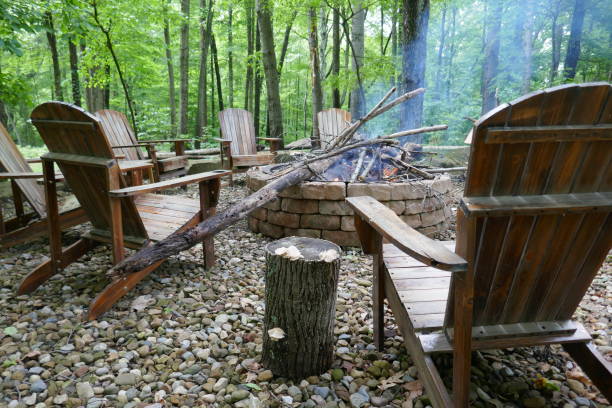istock Low angle view of wooden Adirondack chairs around brick fire pit in forest 1401448227