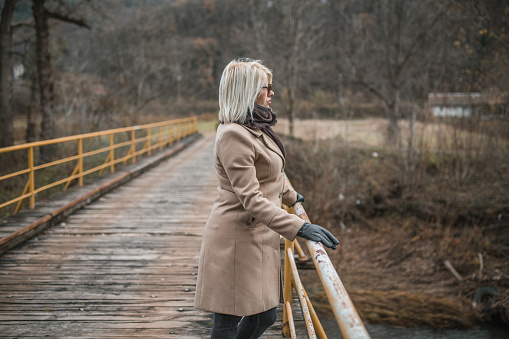 A beautiful young woman standing on a bridge and enjoying a cold winter day in nature