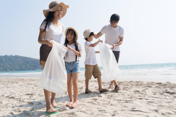 Asian Family volunteer picking up a plastic bottle on a beach with a sea to protect an environment stock photo