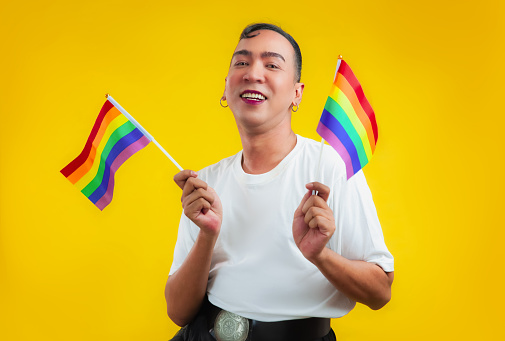Happy gay with pride movement LGBT holding Rainbow flag isolated yellow background. lgbtq+ photo concepts