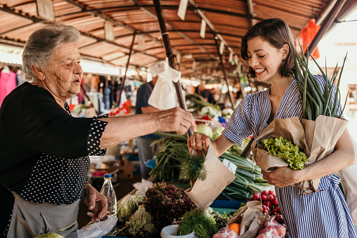 Shot of a beautiful young woman buying fresh vegetables from a senior female seller in the market. Senior woman selling vegetables to a young customer. Real life concept