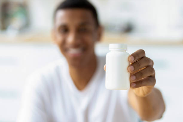 Happy young african american man holding capsules and open bottle. Painkiller, headache medication or vitamins concept stock photo