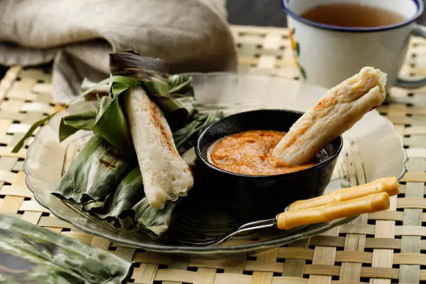 Photo of Otak-otak Tengiri with Peanut Sauce, Made from Fish and Flour,  Wrap with Banana Leaves, on Wooden Table