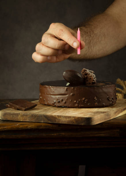 istock Hand holding candle over chocolate cake against gray background 1401467412