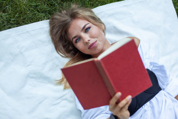 a woman reads a book by the pool enjoying the sun shining on her
