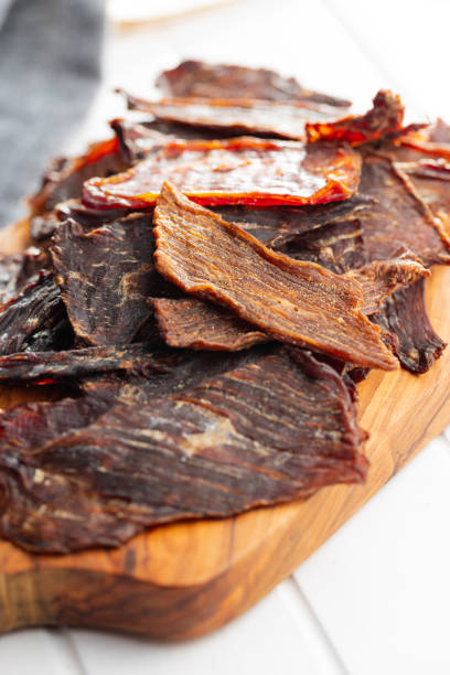 istock Beef jerky meat. Dried sliced meat on wooden cutting board. 1401471862