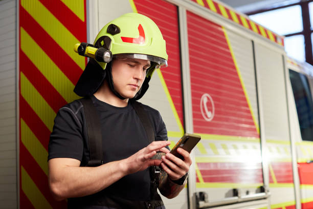 istock Portrait of a firefighter standing in front of a fire engine. Fireman using smart phone 1401472066